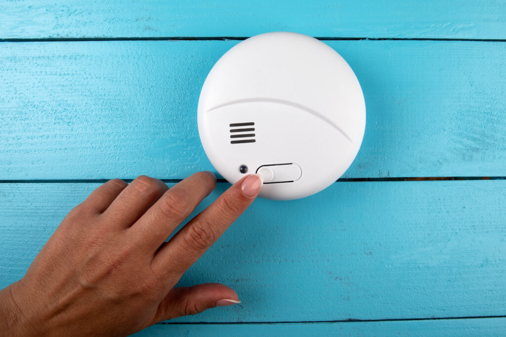 Smoke detector. Woman's finger presses the test button. Smoke, fire alarm.