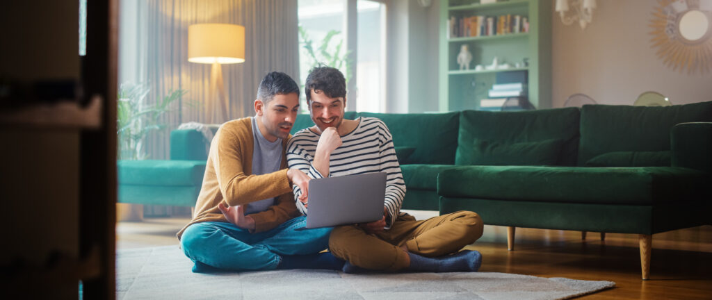 Couple Using Laptop Computer, while Sitting on a Living Room Floor in Cozy Stylish Apartment. 