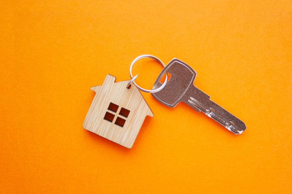 Key and house shaped keychain arrangement on orange background. 