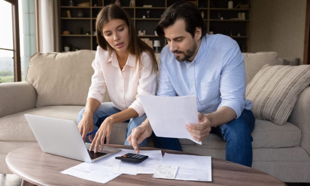 A couple sitting on a sofa reviewing bills and using a laptop and calculator while planning property and budgeting decisions related to the 2025 Budget changes.