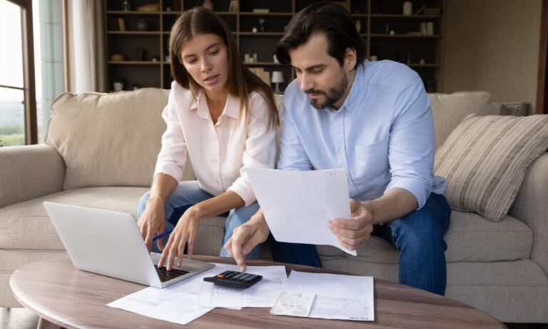 A couple sitting on a sofa reviewing bills and using a laptop and calculator while planning property and budgeting decisions related to the 2025 Budget changes.