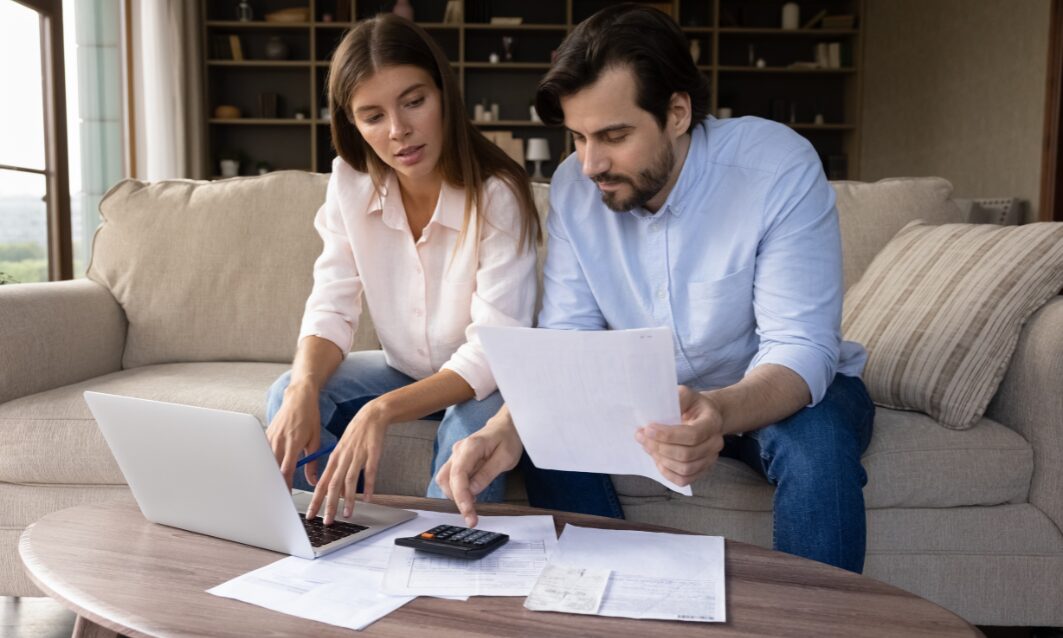 A couple sitting on a sofa reviewing bills and using a laptop and calculator while planning property and budgeting decisions related to the 2025 Budget changes.
