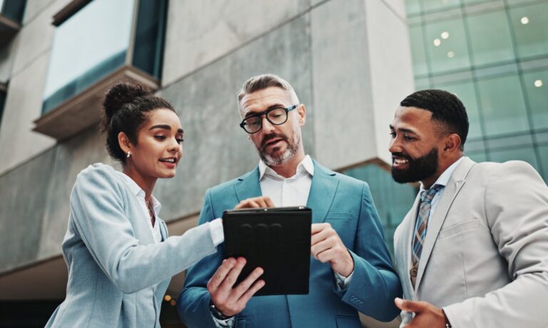 Estate agents discussing property market information on a tablet outside a modern building in Leicester.